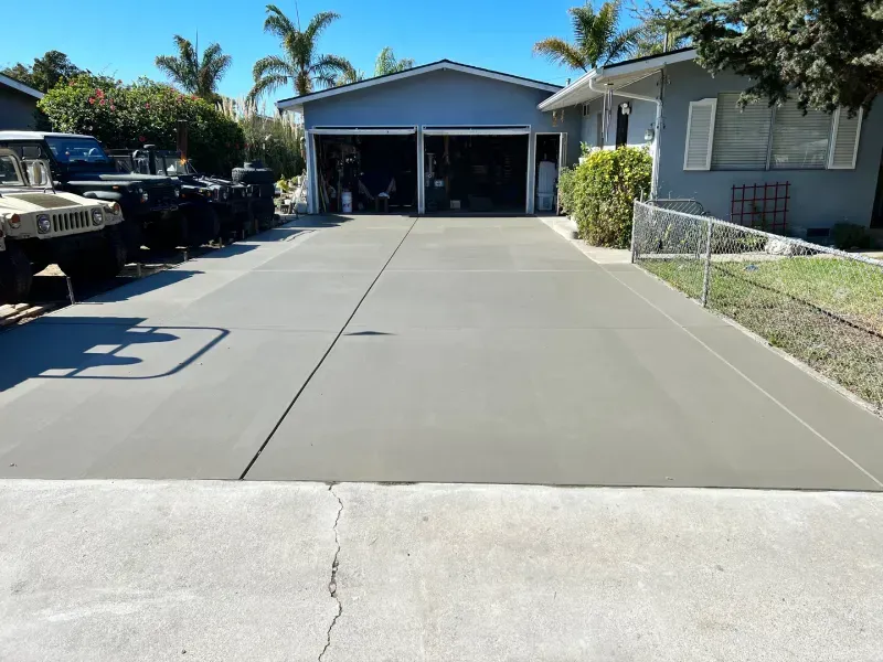 Freshly poured concrete driveway in front of a blue garage and house, sunny day.