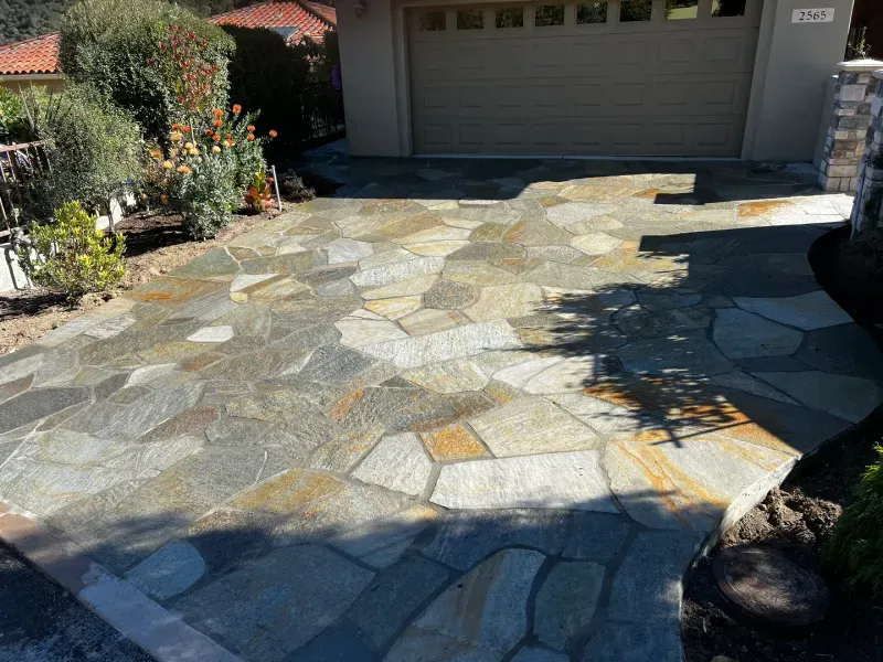 Flagstone driveway leading to a garage. The stones are in shades of grey, brown, and gold.