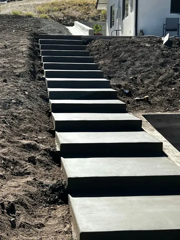 Concrete outdoor staircase leading up a sloped hill towards a building, with exposed dirt on either side.