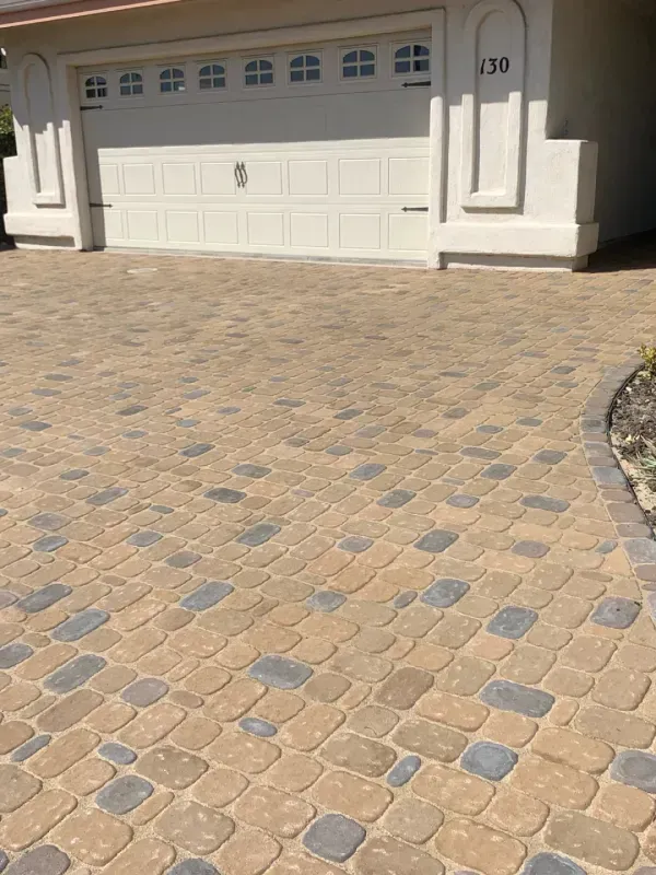 Brick driveway in front of a white garage door with house number 120. Brick color is tan and grey.