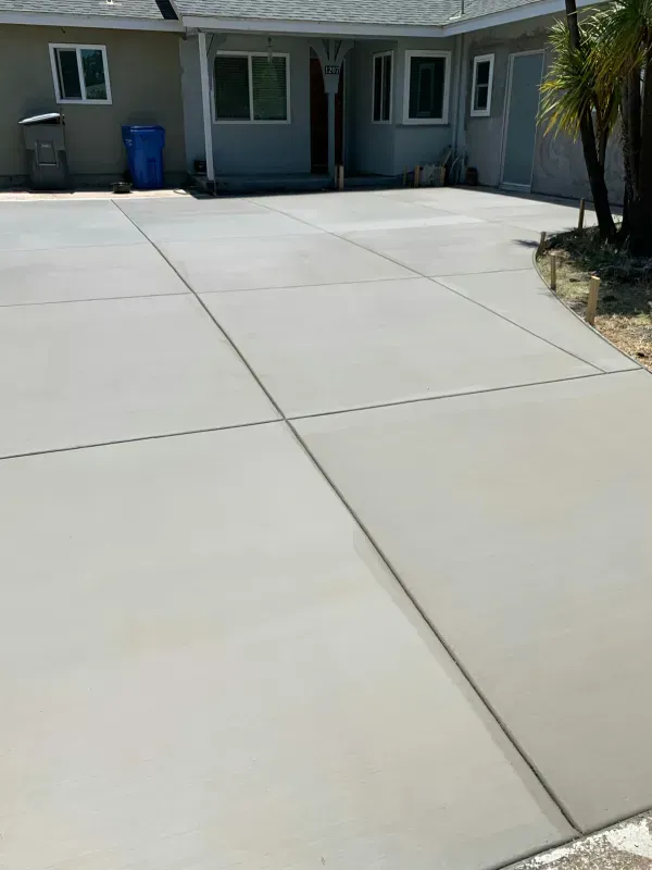 Freshly poured gray concrete driveway with control joints, leading to a house entrance.