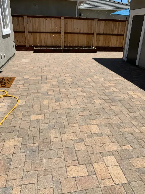 Brick paved patio with wooden fence backdrop. Yellow hose on the left.