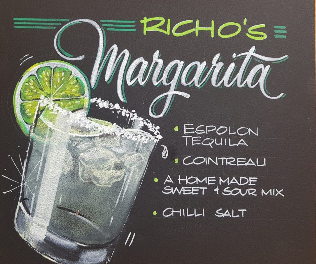 A chalkboard with a drawing of a margarita on it