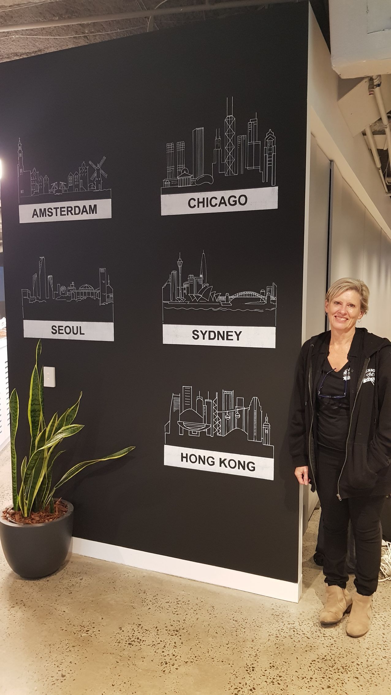 A woman is standing in front of a wall with drawings of cities on it.