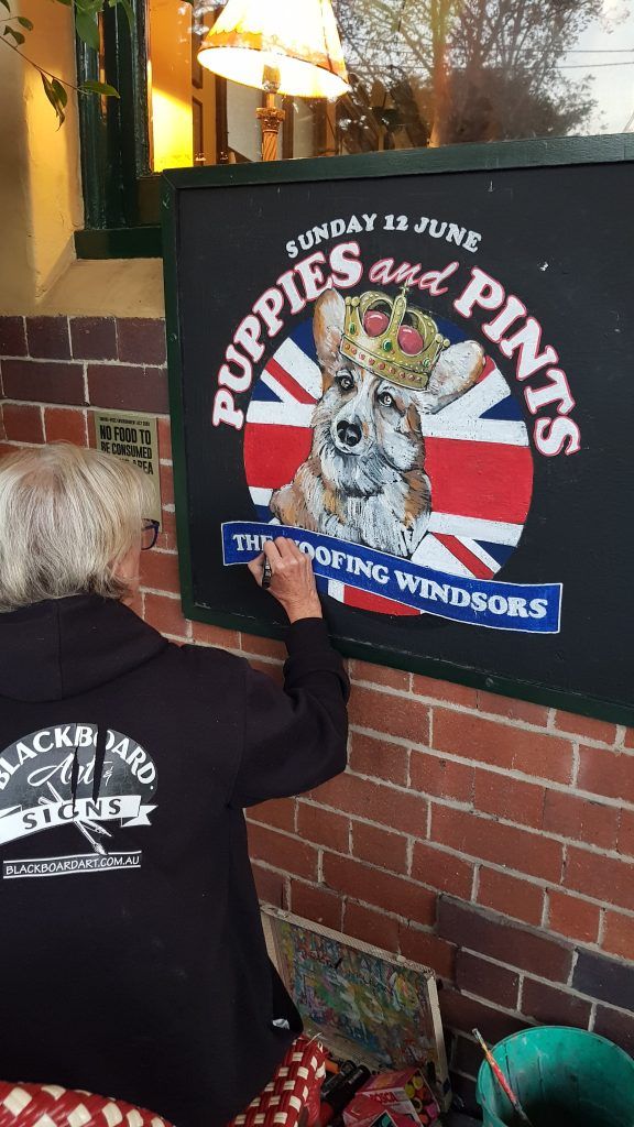 A woman is painting a sign for puppies and pints
