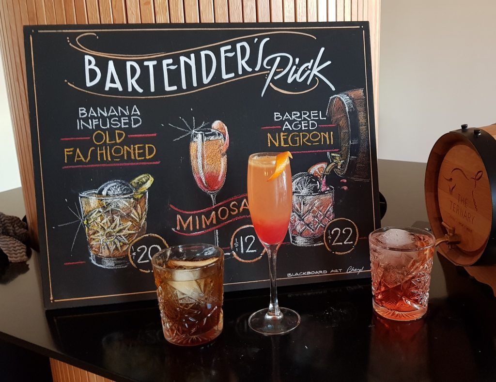 A bartender 's pick chalkboard with three drinks on it