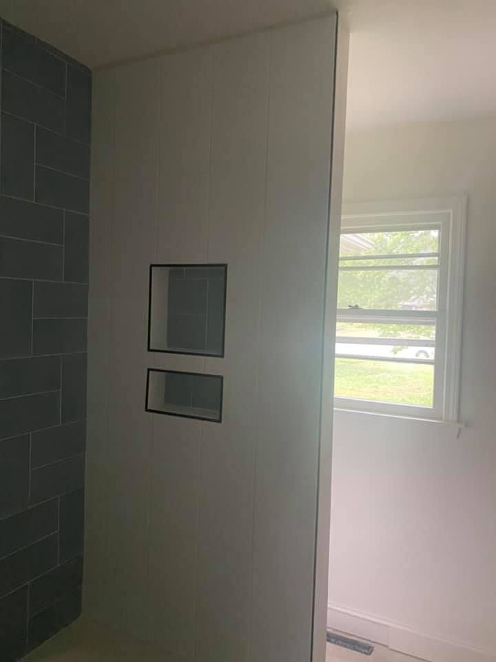 Bathroom wall with two built-in recessed shelves. Dark tiled shower on the left, window on the right.