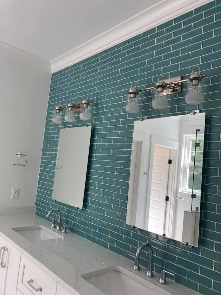 Bathroom with teal tiled wall, two mirrors above sinks, and three-light fixtures.