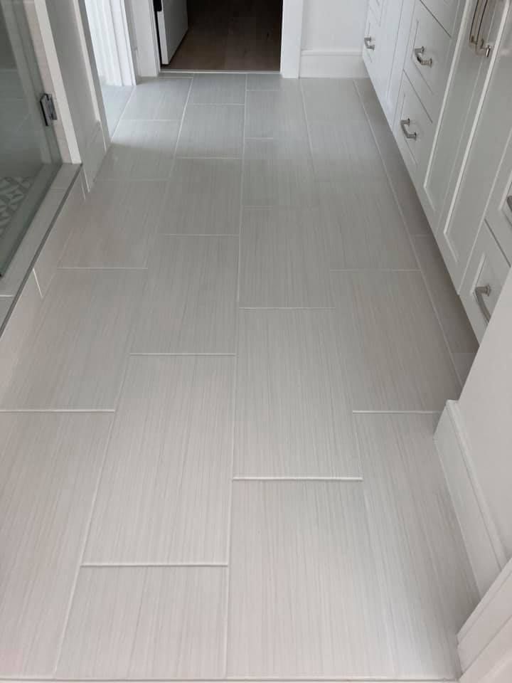 Light gray tile floor in a bathroom with white cabinets, doorway, and shower.