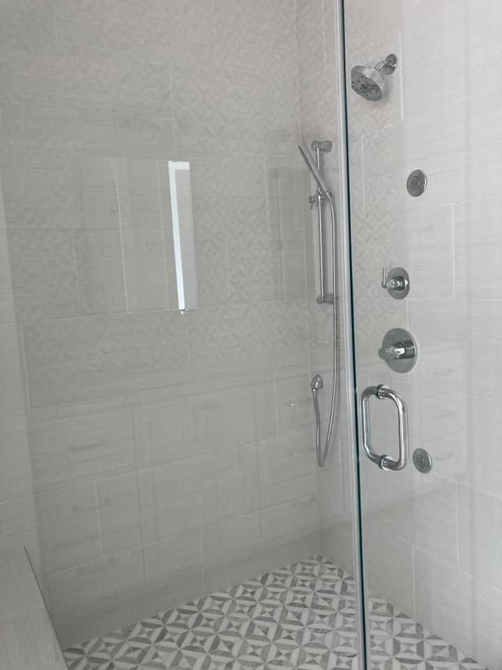 A modern, white-tiled shower with a glass door, silver fixtures, and patterned floor tiles.