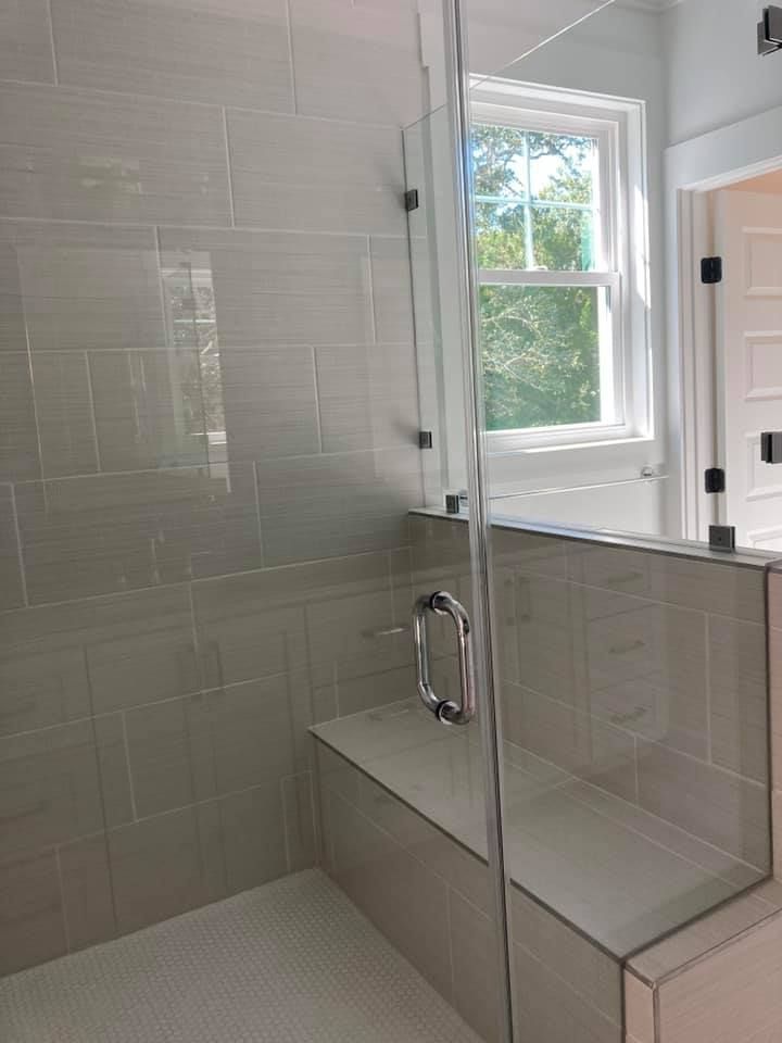 Shower with glass door, tiled walls and a bench. A window is visible in the background.
