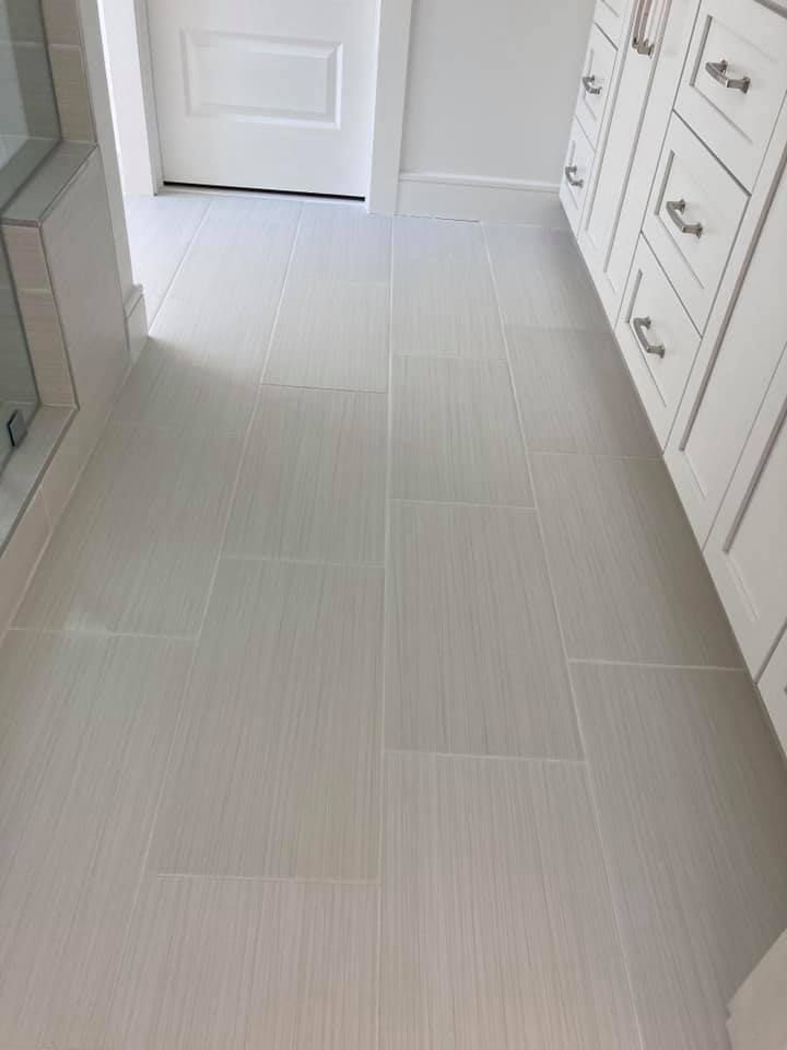 Light gray tiled bathroom floor with white vanity and door.