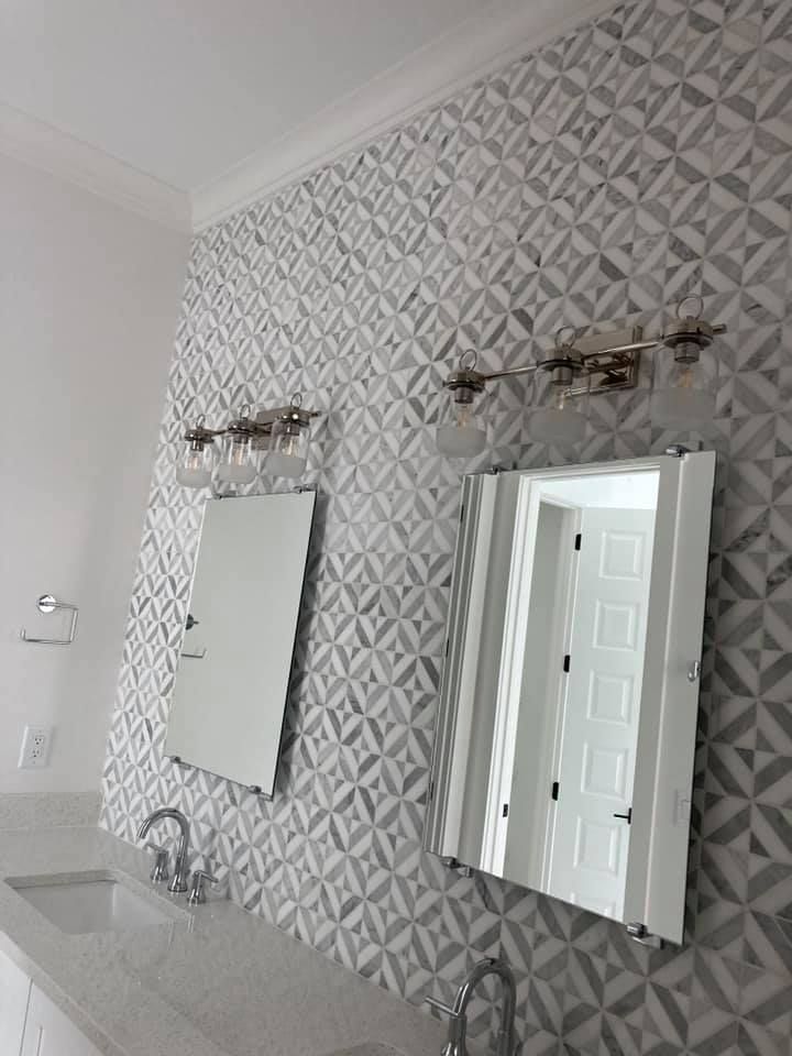 Bathroom with patterned gray and white tile wall, mirrors, and light fixtures.