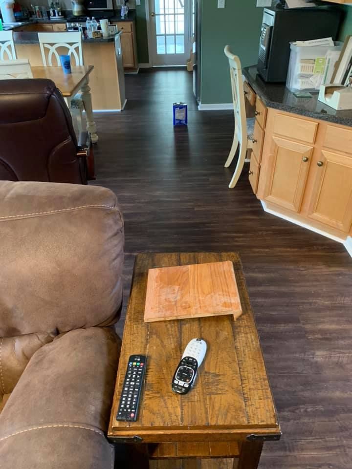 Living room with brown furniture, wood floor, and kitchen visible in background.