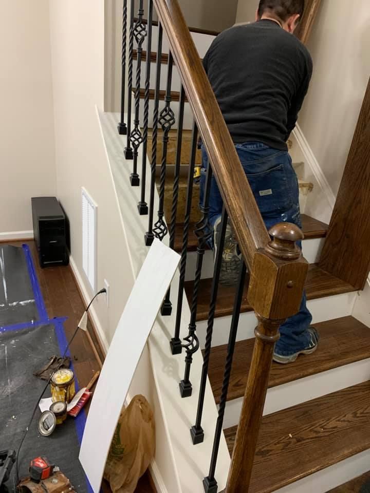 Person installing stair treads; staircase with black iron spindles; work tools are visible.