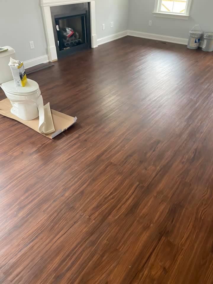 Dark wood-look flooring in a room. Fireplace in the background, paint cans near the window.