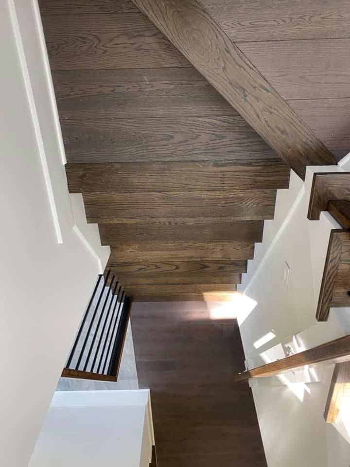 Wooden staircase with dark treads and white walls, leading down. Railing on one side.