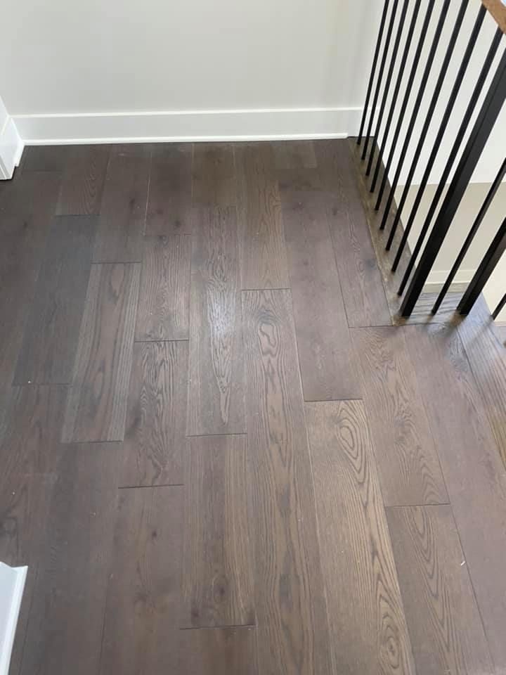 Dark gray hardwood floor with a white baseboard and black railing.