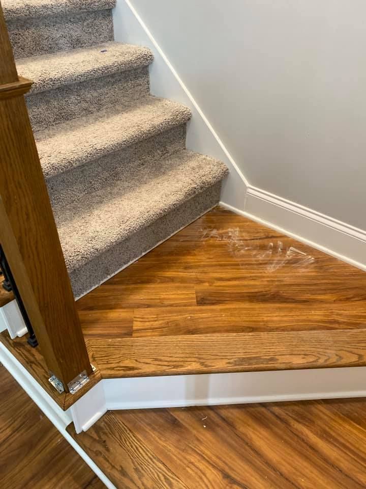 Wooden staircase with carpeted steps, against a gray wall and a brown floor.