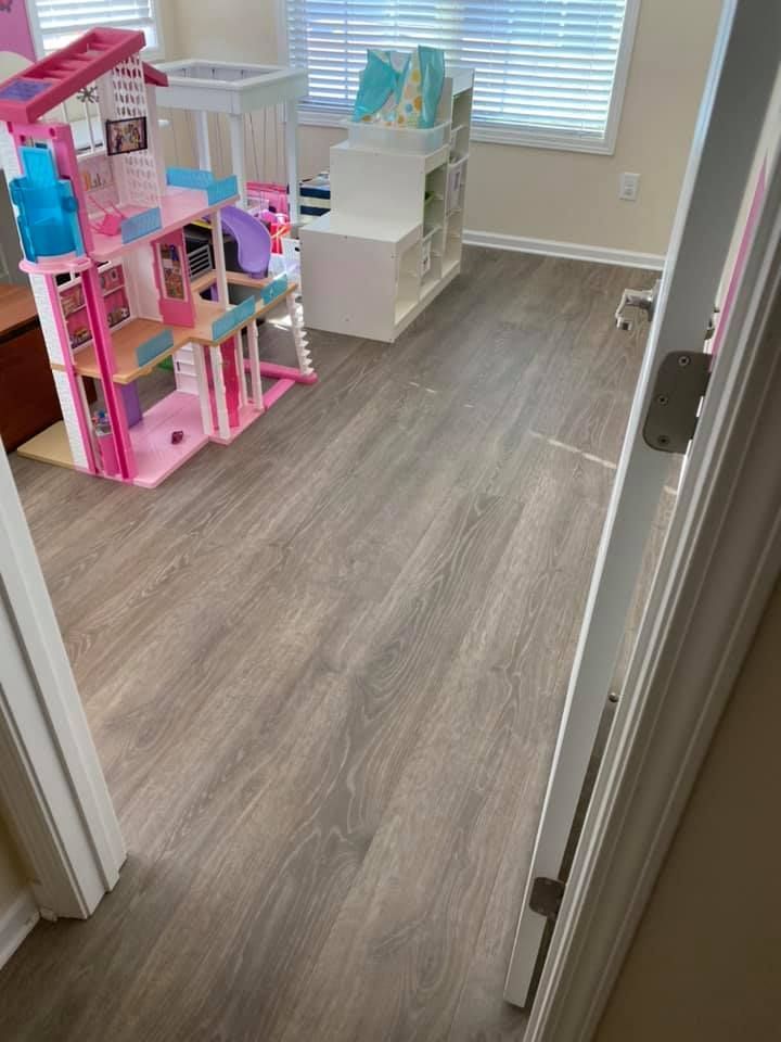 A room with gray wood-look flooring and a Barbie dreamhouse.