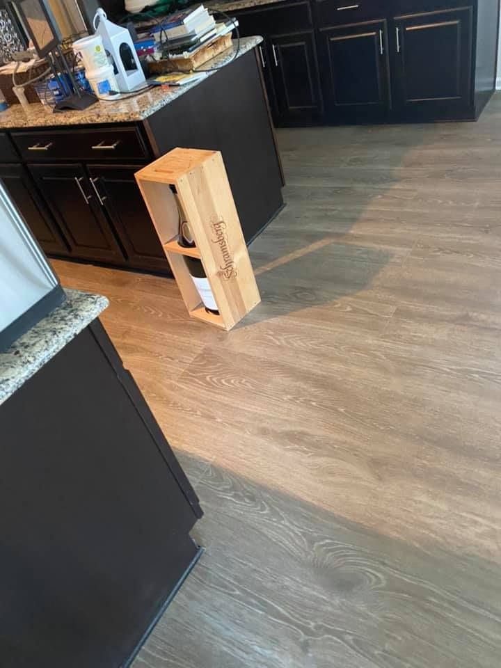 Kitchen with dark cabinets, light wood-look flooring. A wooden wine box with a bottle inside sits on the floor.