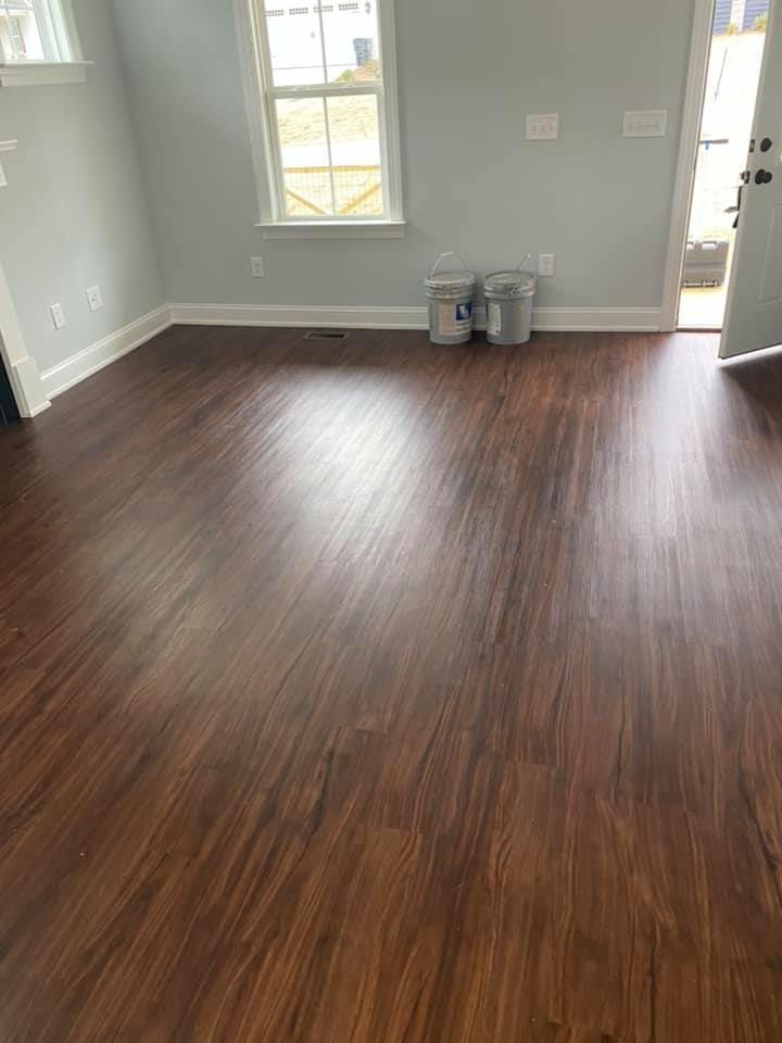 Dark wood laminate flooring in a room with light gray walls, a white window, and paint buckets.