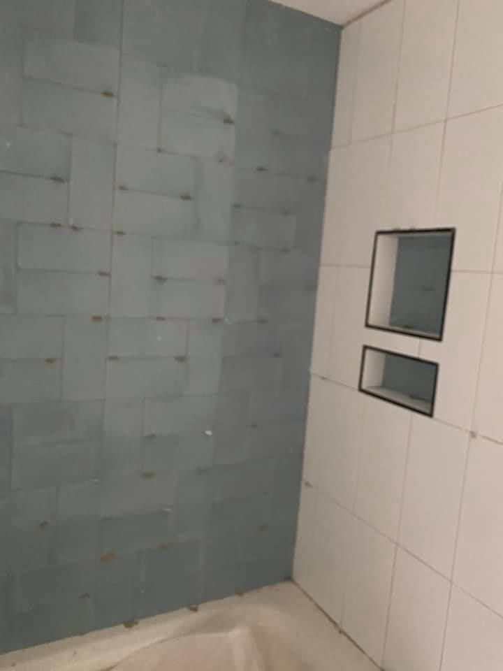 Bathroom corner with blue-gray tiled wall and white tiled wall with recessed shelves; light tan tub visible.