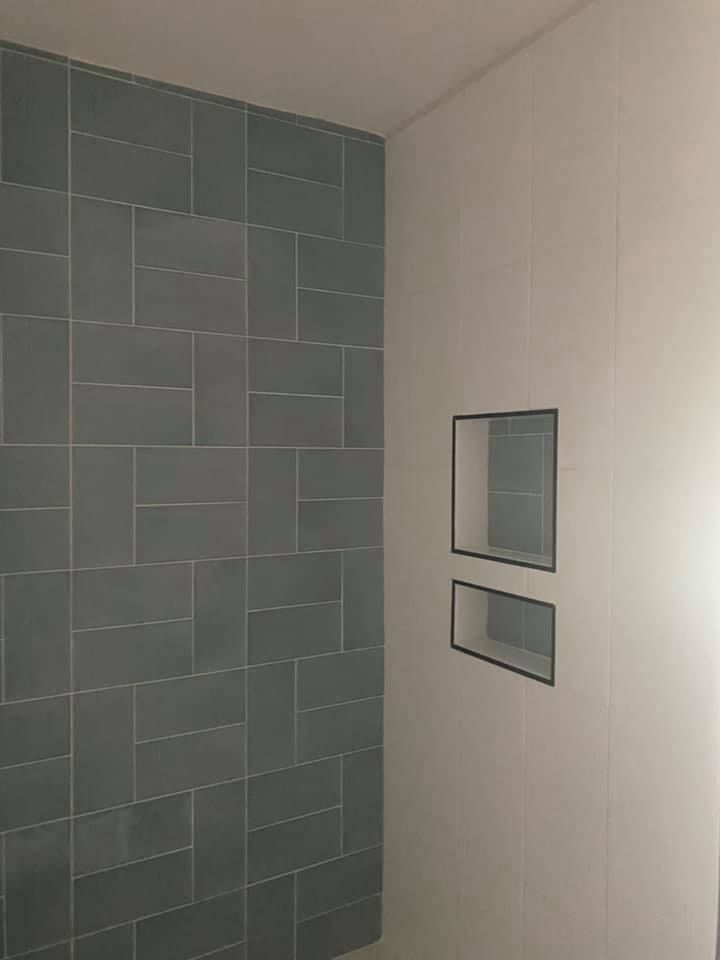 Gray tiled shower wall with built-in rectangular niches, next to a white wall.