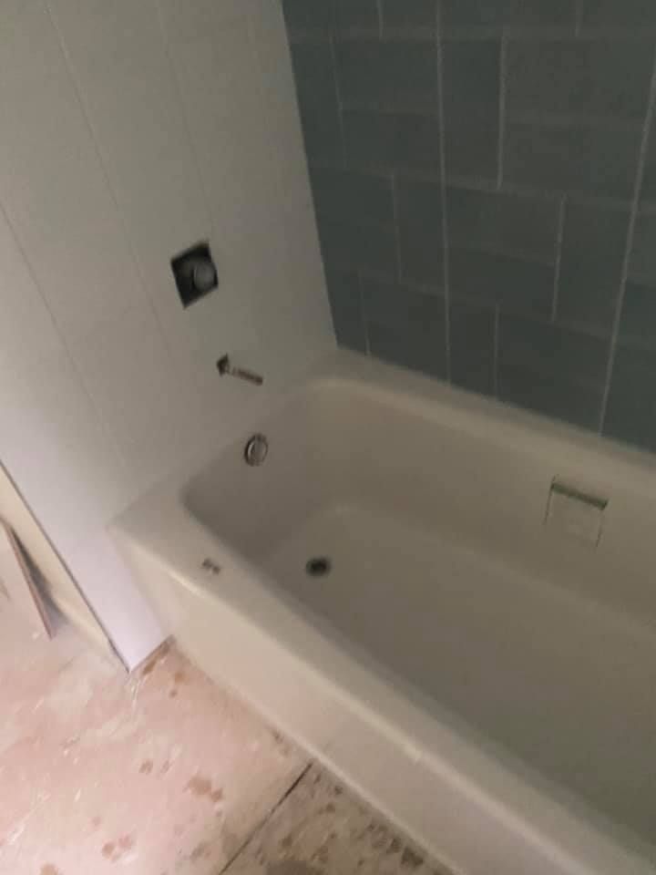 White bathtub with blue tiled wall, silver faucet fixtures in bathroom.