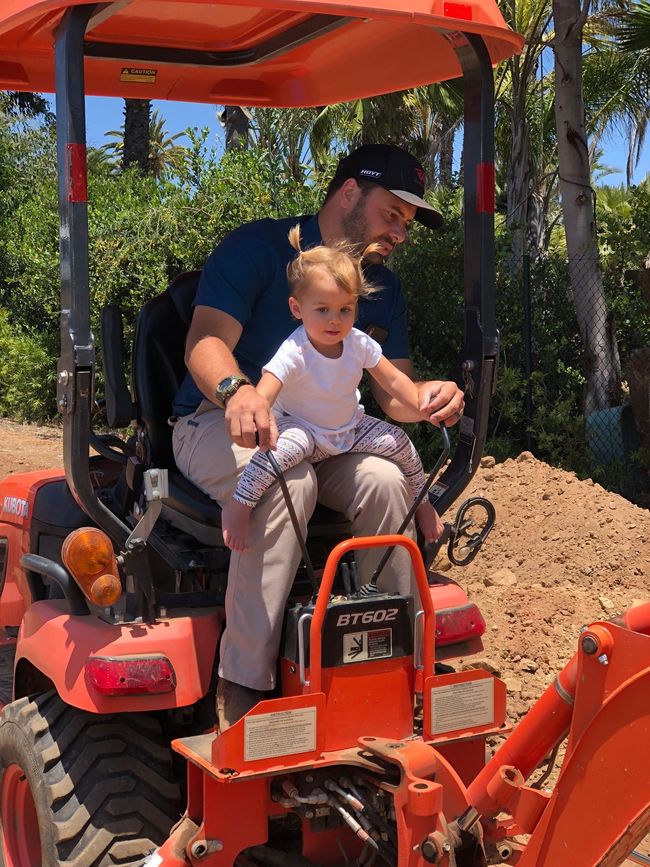 Peter  and a little girl are sitting on an orange tractor.