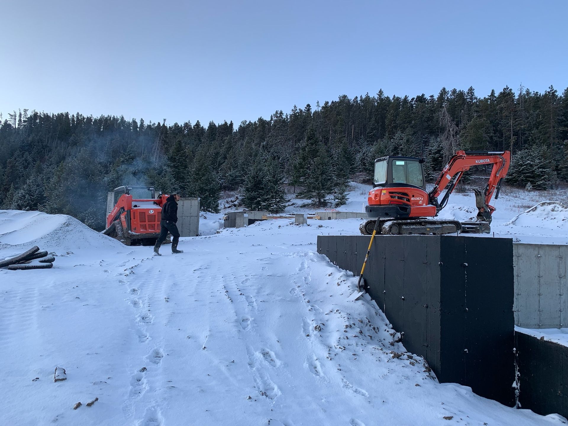 A man is standing next to an excavator in the snow.