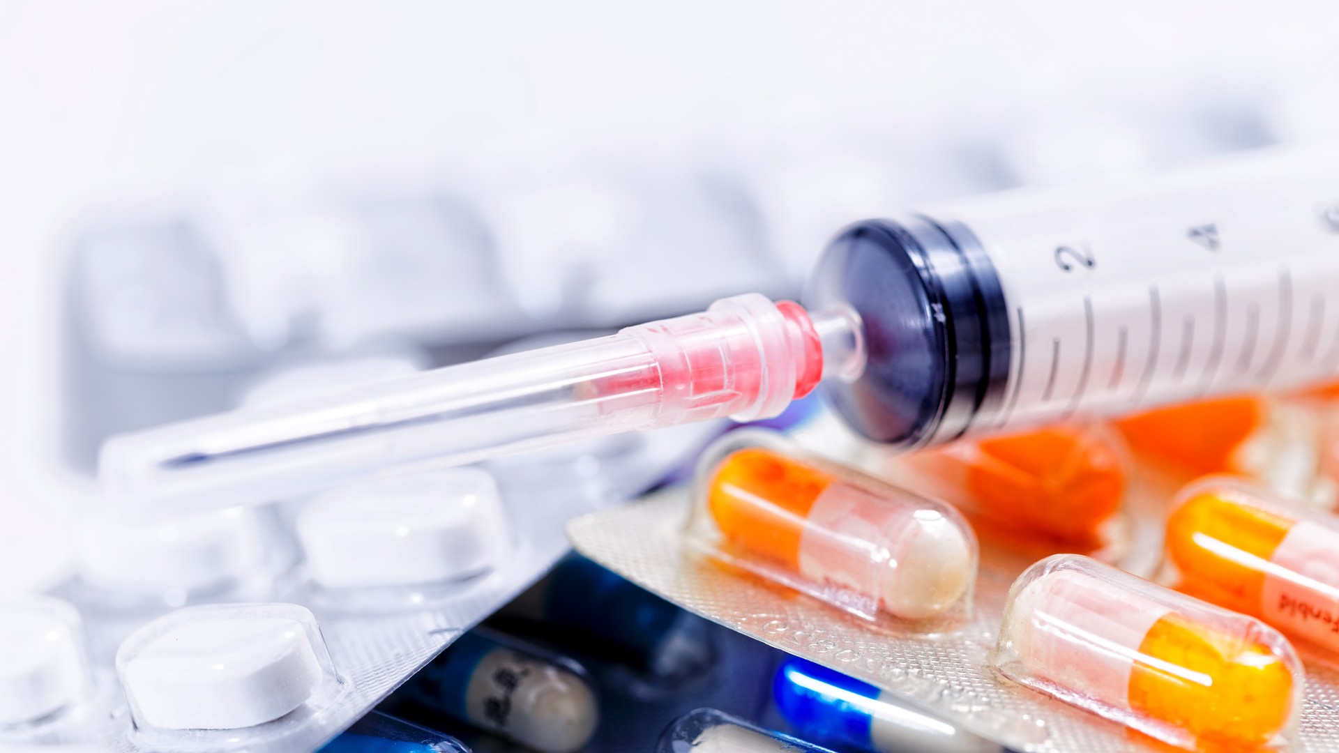 A syringe is sitting on top of a pile of pills and capsules.