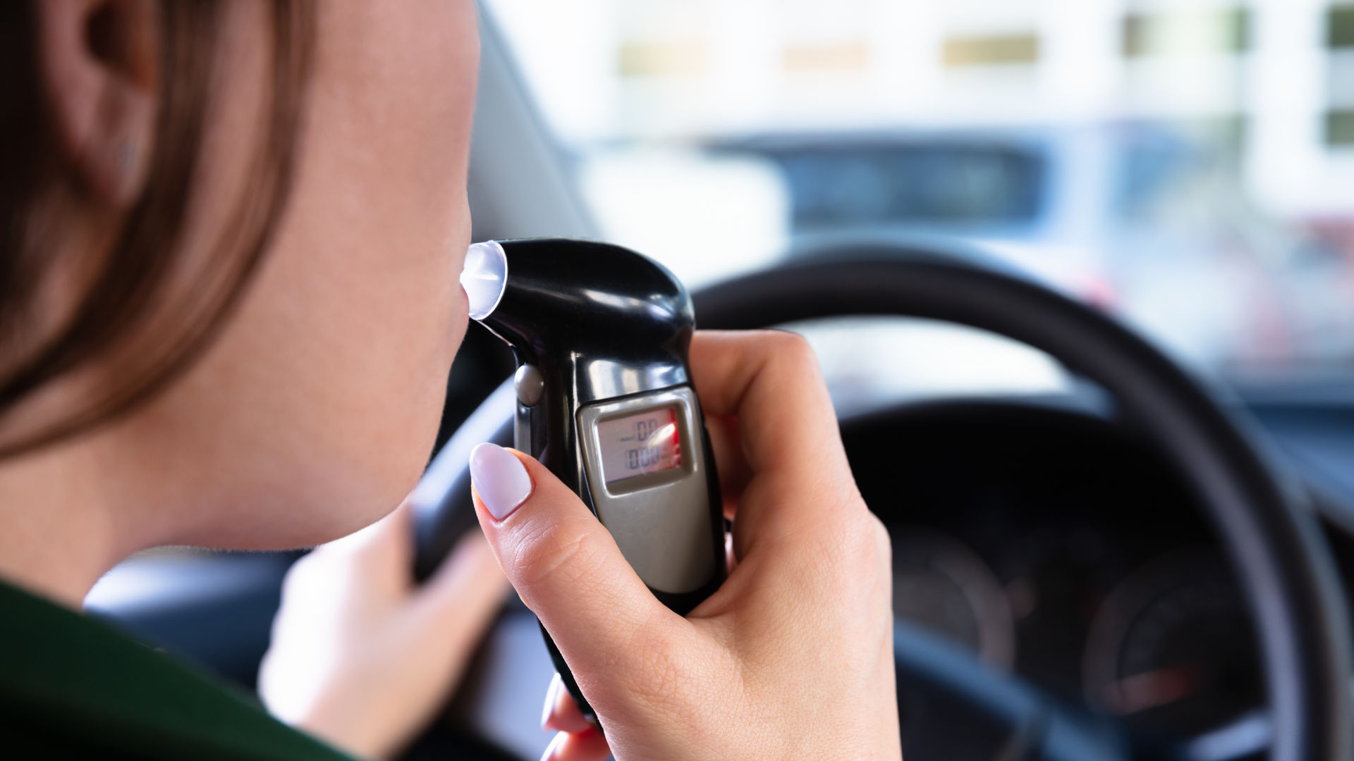 A woman is taking a breathalyzer in her car.