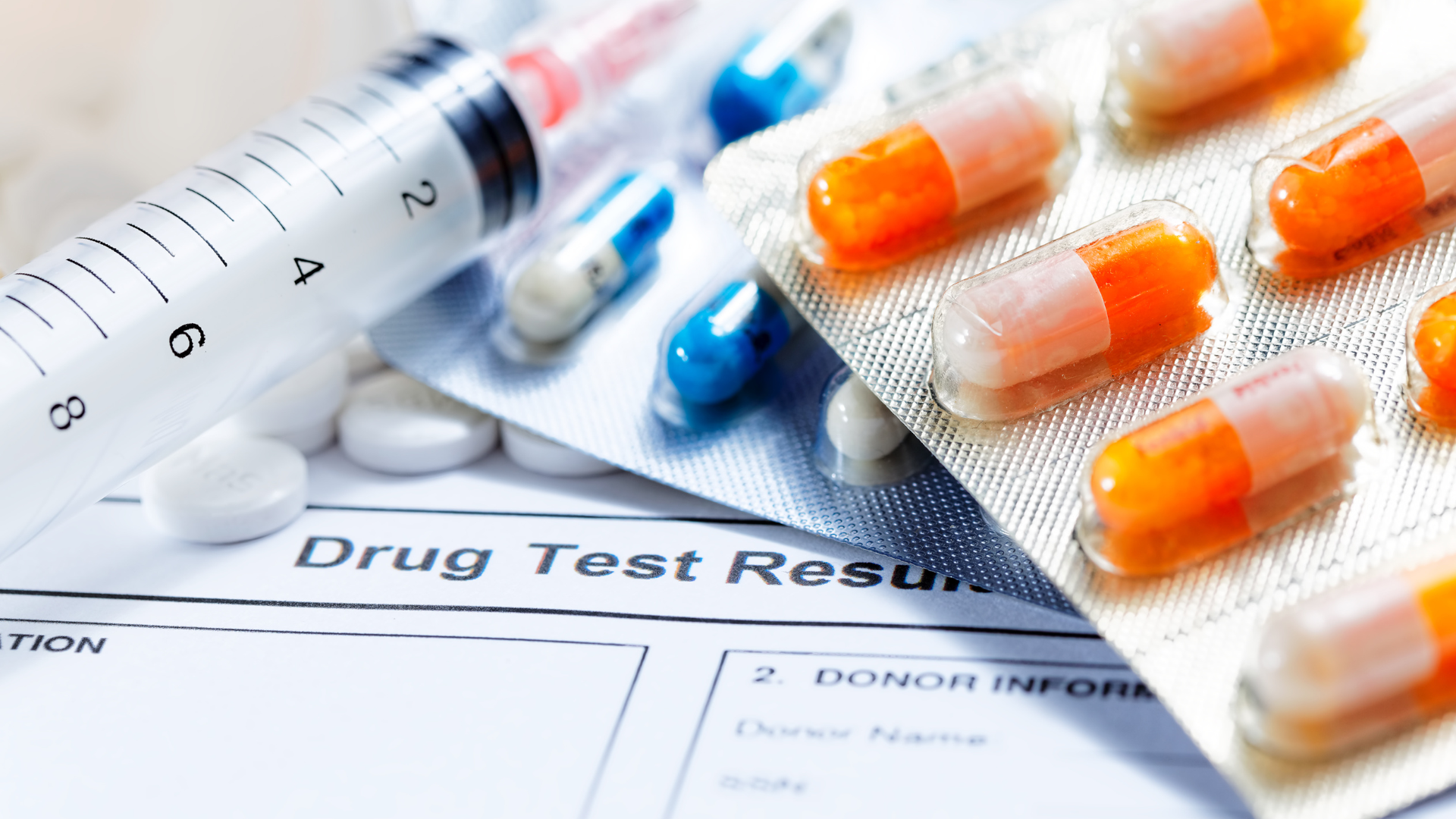 A syringe and pills are on top of a drug test result
