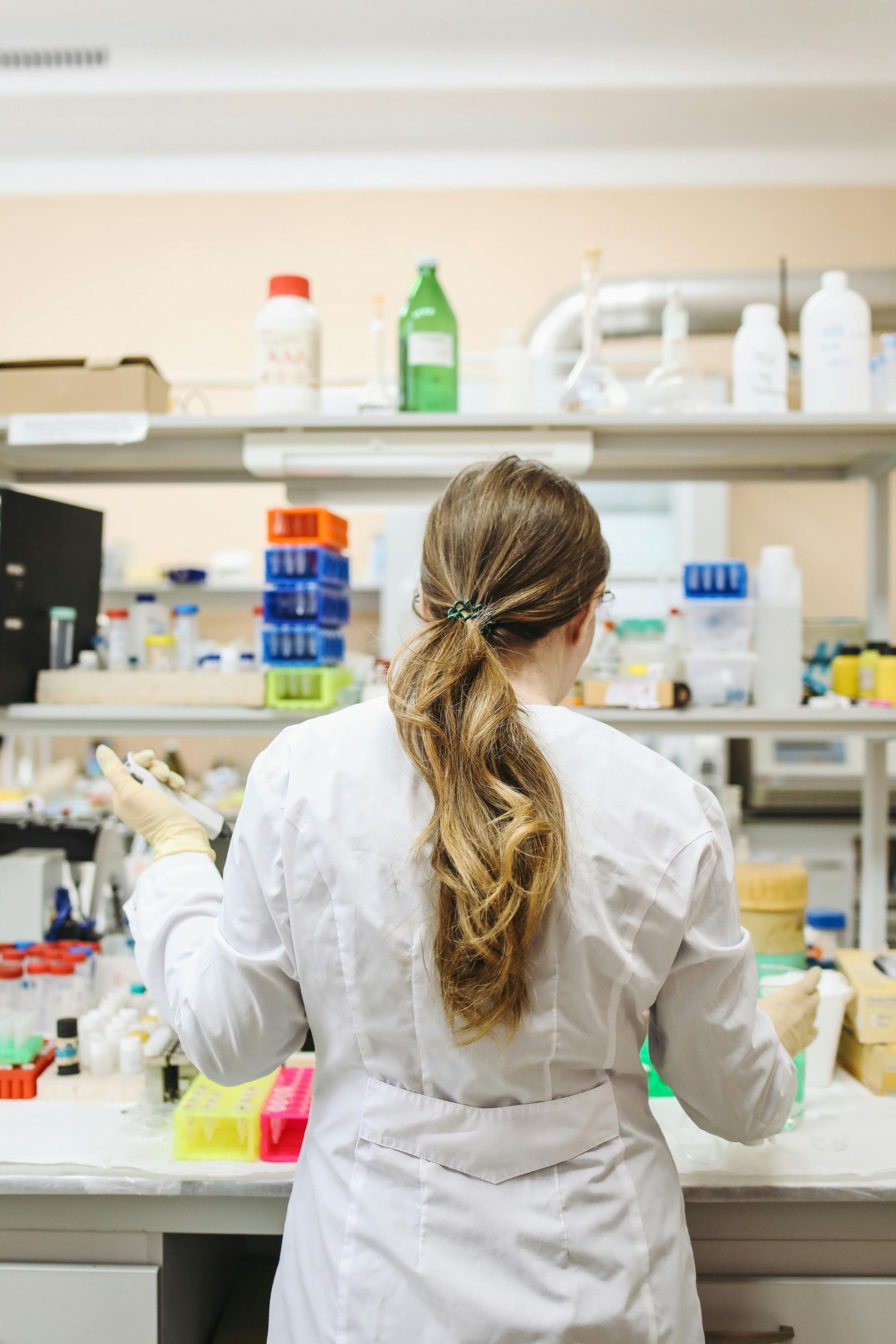 Scientist in lab coat, examining beakers and lab equipment in a laboratory setting.