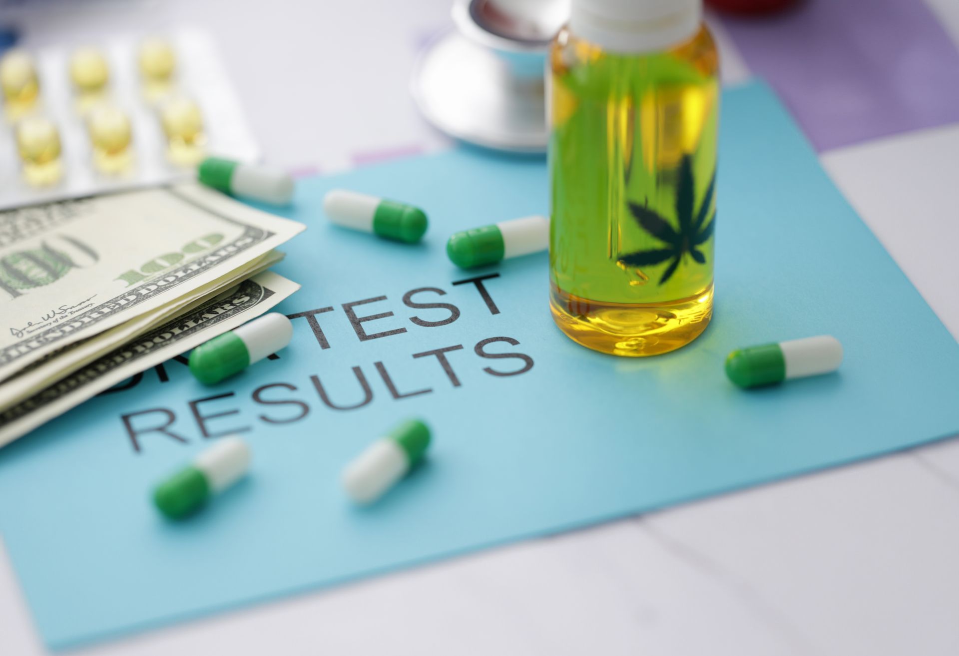 A bottle of cannabis oil, green-and-white capsules, money, and a stethoscope placed on a document labeled Test Results.