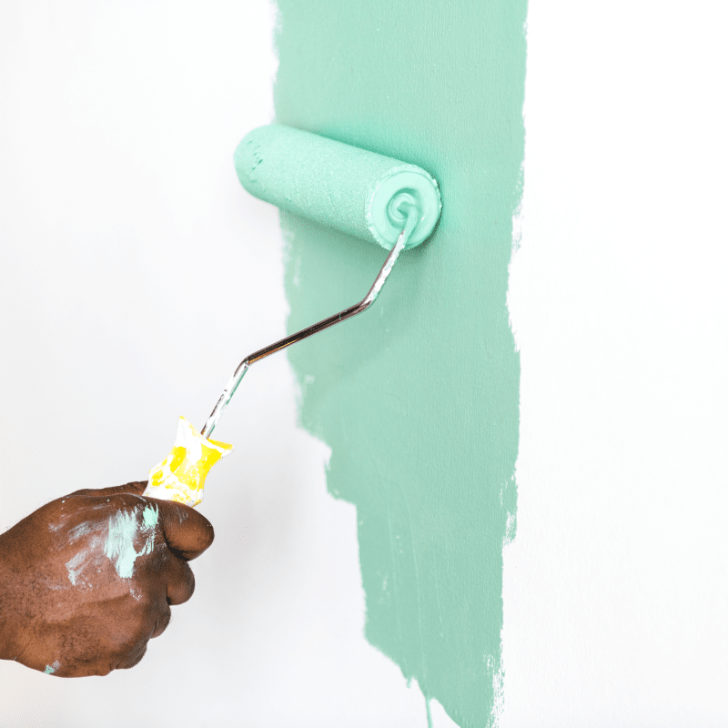 Hand painting a white wall with a green paint roller, leaving a vertical stripe.