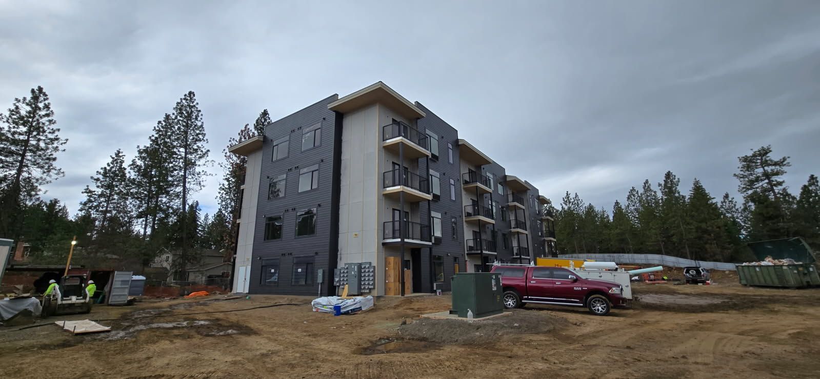 Construction site with a partially built multi-story apartment building. Workers are present; a red pickup truck is parked nearby.