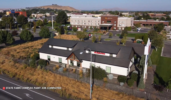 A commercial building with tan stucco walls, black awnings, and large windows.