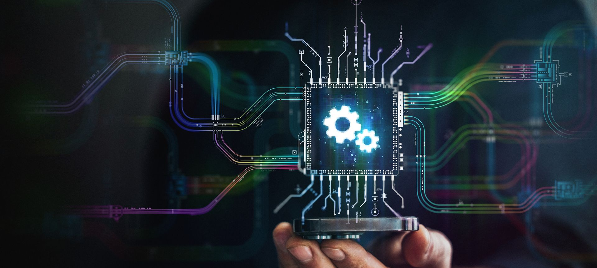Hand holding a glowing microchip with gears, circuitry, and colorful lines on dark background.