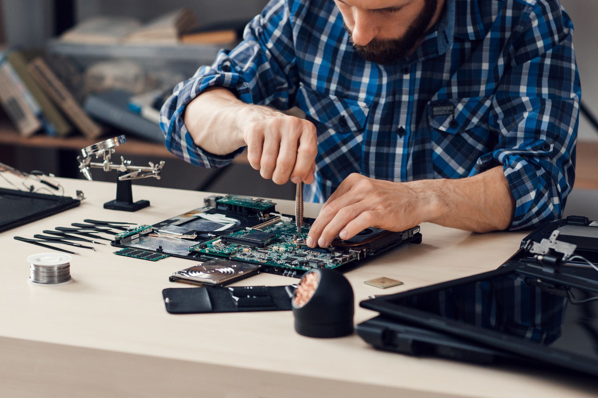 Man fixing computer circuit board with tools on a table.