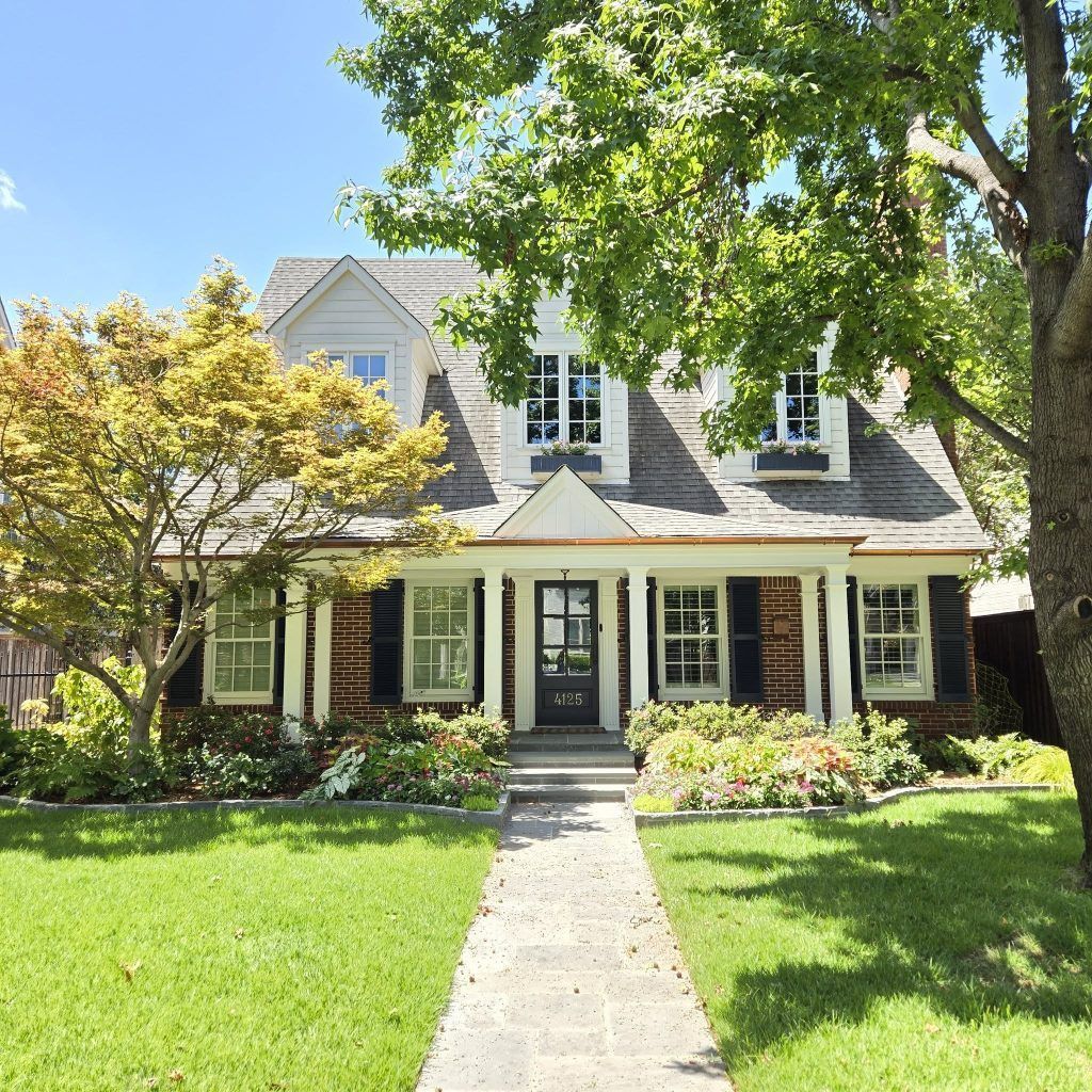 Charming two-story house with brick facade, shutters, and a walkway through a lush green lawn.