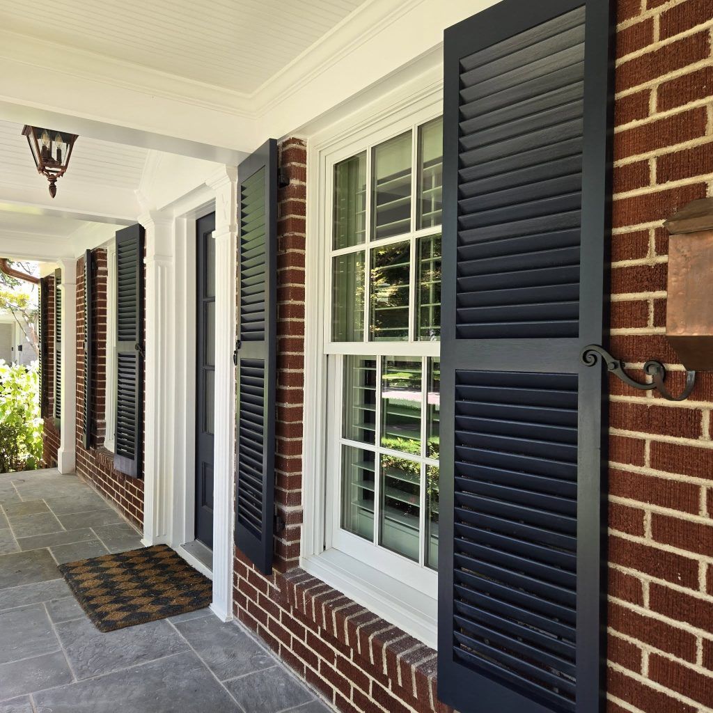 Exterior of a brick building with black shutters on white windows and a covered porch.