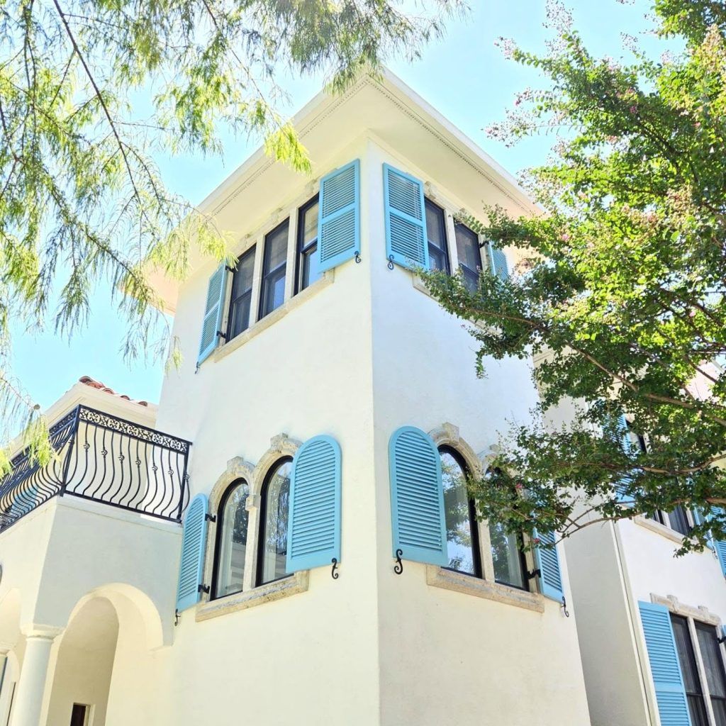 White stucco house with light blue shutters and black framed windows, under a blue sky.