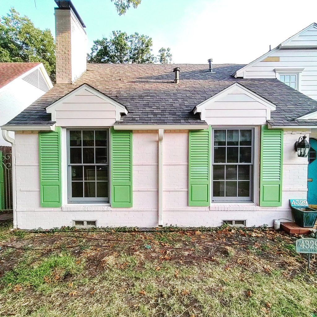 Small pink house with green shutters and a dark gray roof.