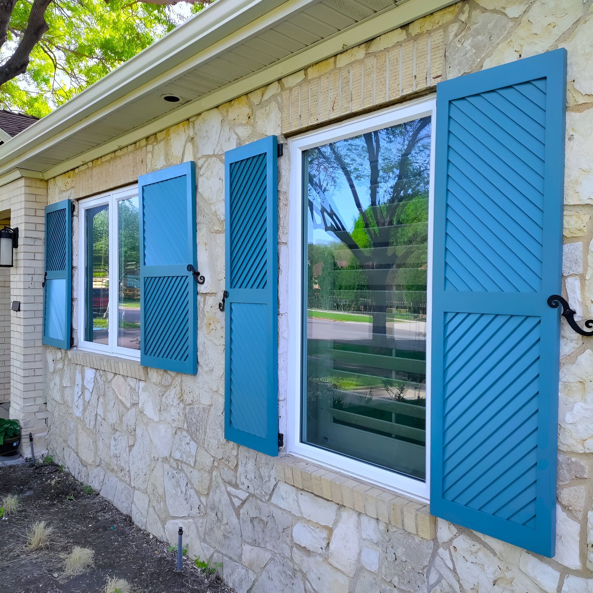 Blue shutters on a stone house. Windows are visible. Green plants are in front of the house.