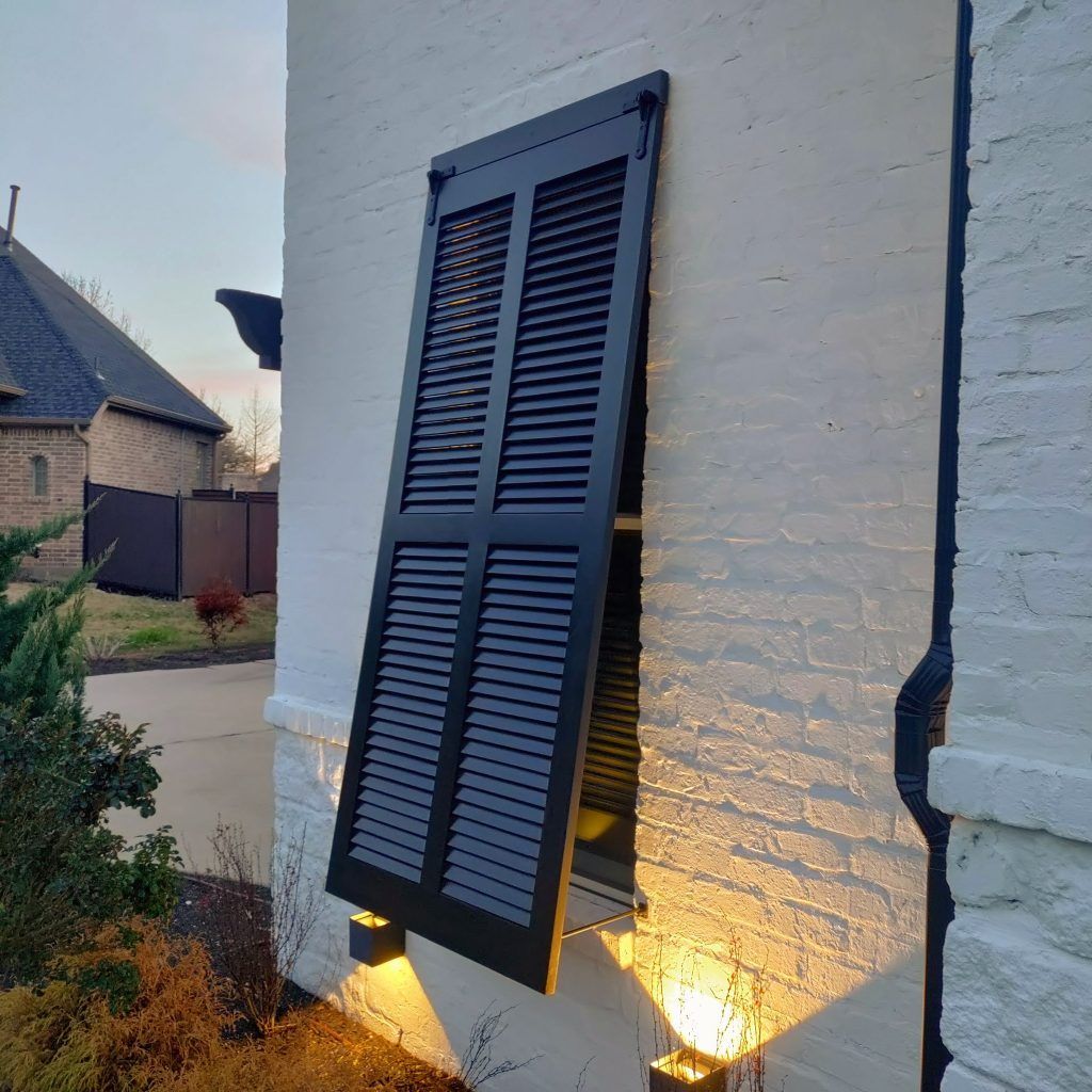 Black shutter on a white brick building, partially open. Window is visible.