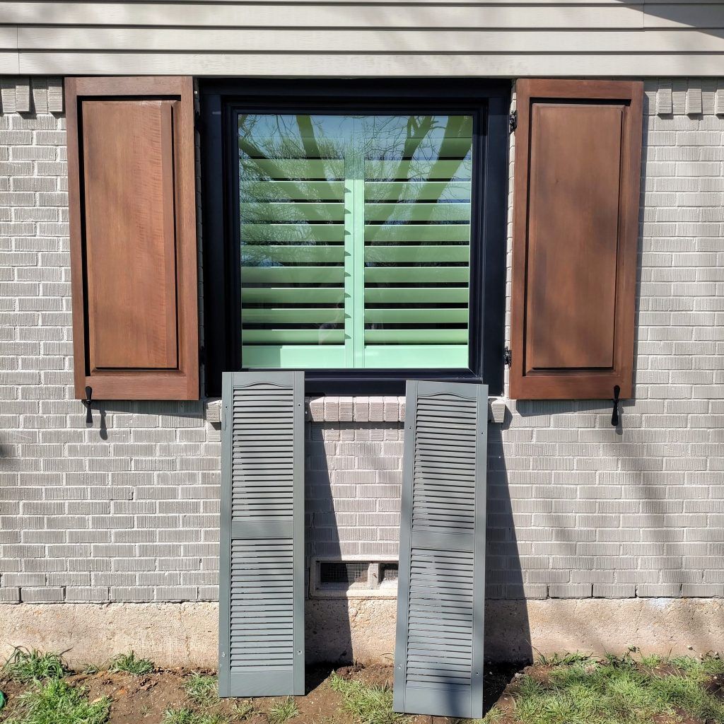 Window with closed interior shutters and open exterior shutters, along with two detached shutters on a brick wall.