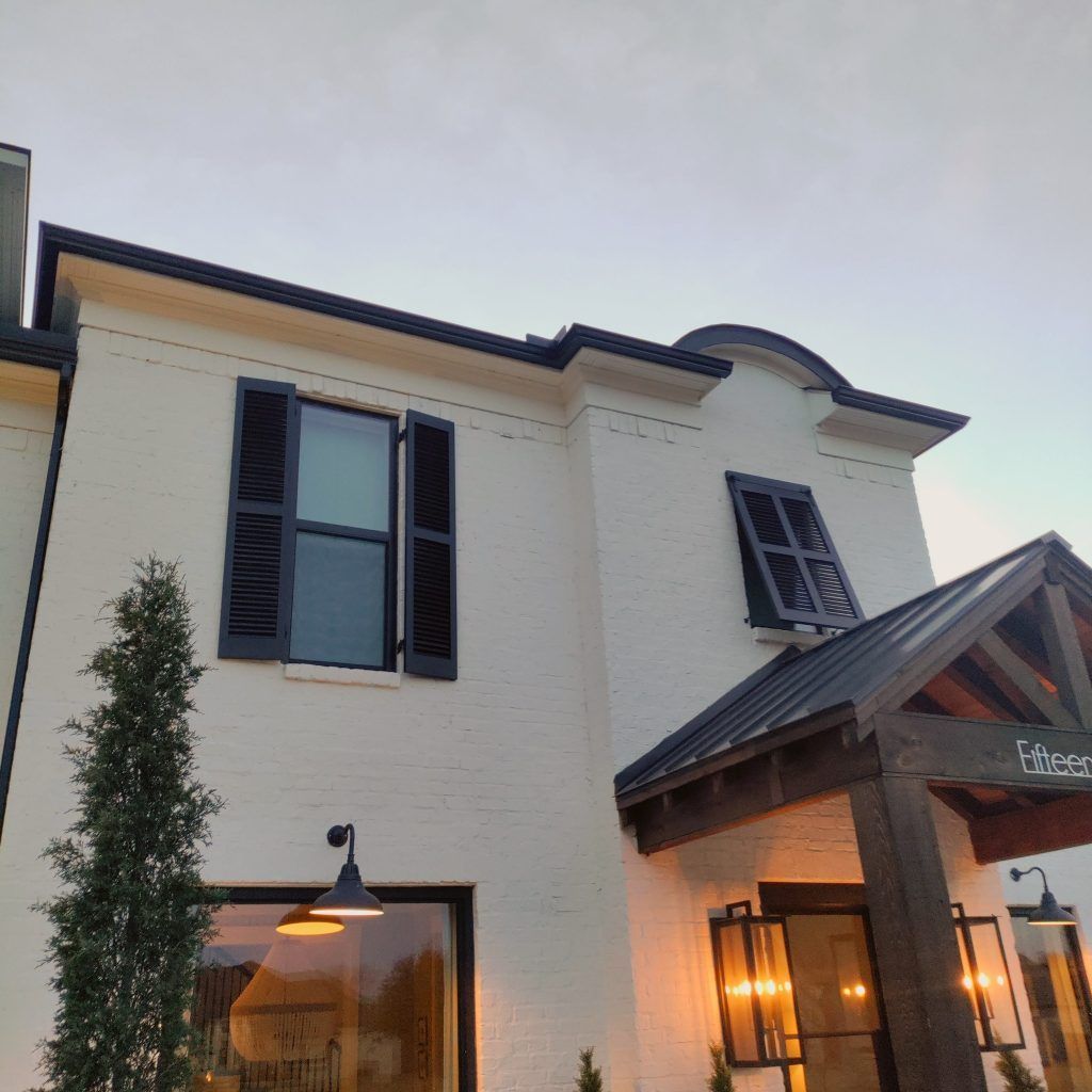 White brick house with black shutters, trim, and a wooden entrance under an evening sky.
