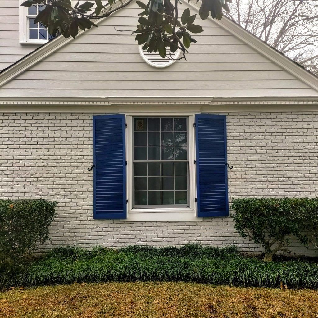 White brick house with blue shutters, a window, and manicured landscaping.